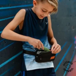 Young boy inserting Epipen into insulated compact waist holder pouch with carabiner ID card, wearing as fanny pack for allergy safety